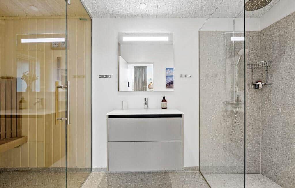 Badezimmer mit Dusche, Waschbecken und Spiegel. Glaswand trennt Dusche vom Rest.