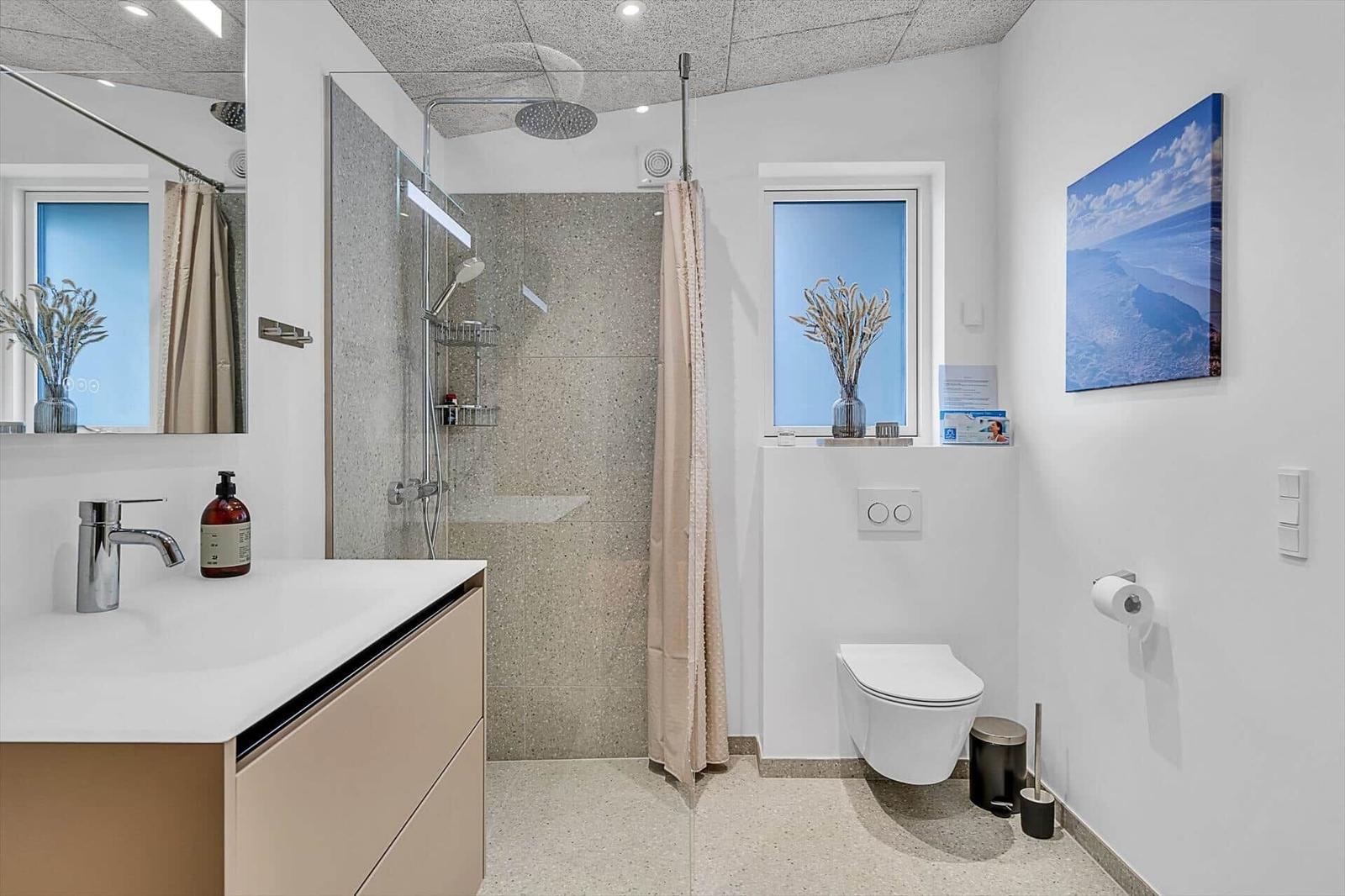 Badezimmer mit Dusche, Waschbecken und Toilette. Fenster und Wandbild mit Landschaft.