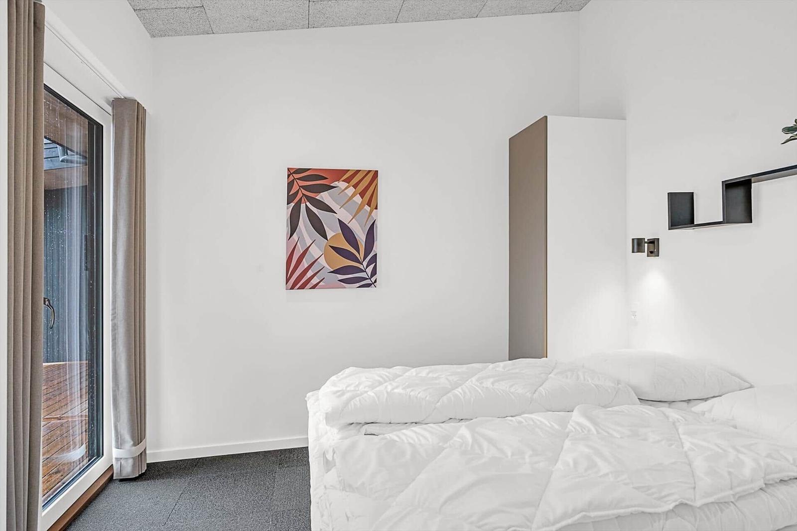 Schlafzimmer mit weißem Bett, Wandbild und Glastür zum Balkon.