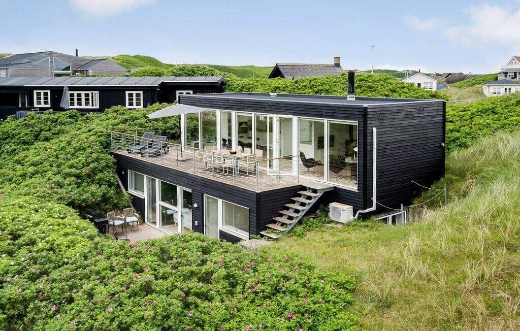 Moderne schwarze Villa mit Terrasse und großem Glasbereich in grüner Landschaft.
