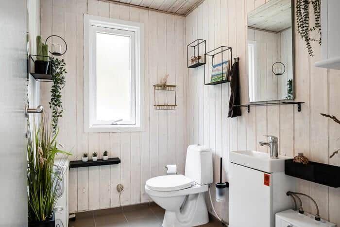 Badezimmer mit Toilette, Waschbecken und Fenster. Holzwände und Pflanzen.