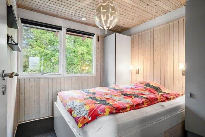 Schlafzimmer mit Bett, Fenster und Holzwandverkleidung.