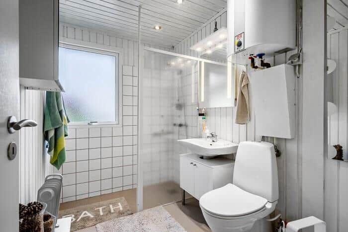 Badezimmer mit Dusche, Waschbecken und Toilette. Fenster, Spiegel und Handtuchhalter sichtbar.