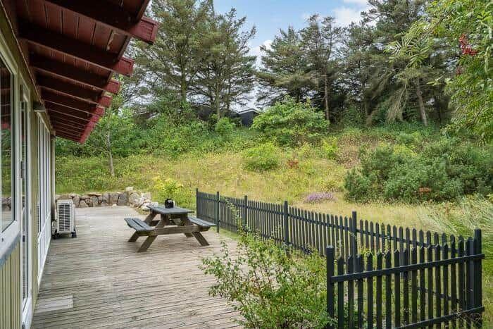 Holzterrasse mit Picknicktisch und Sitzgelegenheit, umgeben von Grün und einem Zaun.