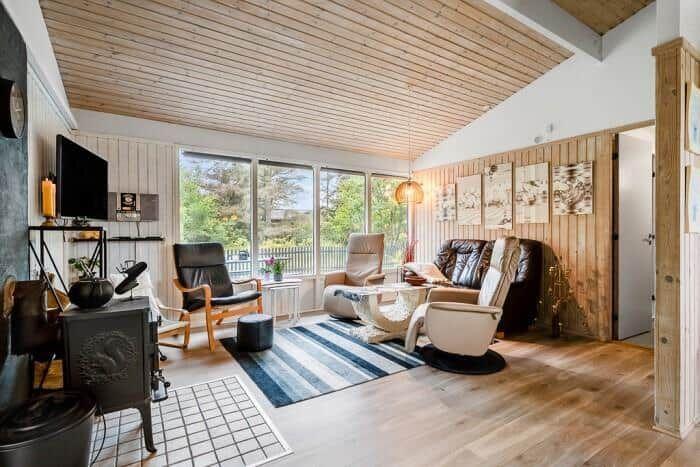 Wohnzimmer mit Holzdecke, großen Fenstern und Sitzgelegenheiten.
