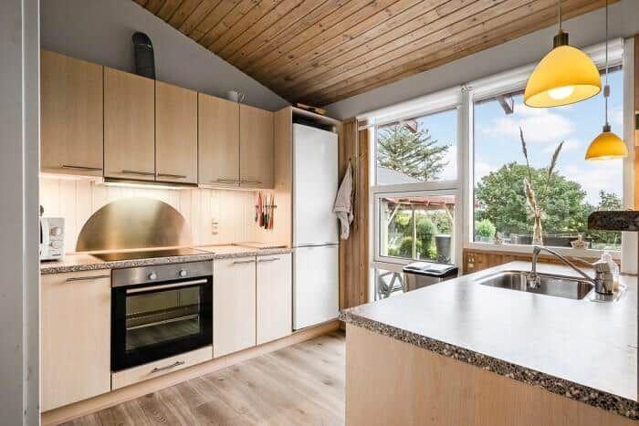 Küche mit Holzdecke, weißen Schränken und Blick auf Garten.