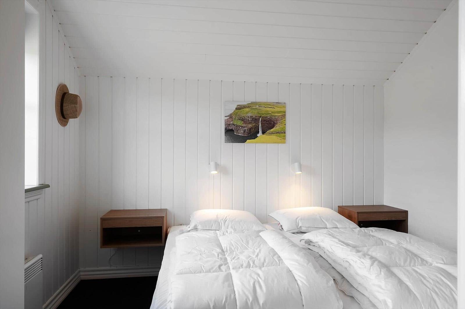 Schlafzimmer mit Doppelbett, zwei Nachttischen und Wandbild. Decke und Wände sind weiß verputzt.