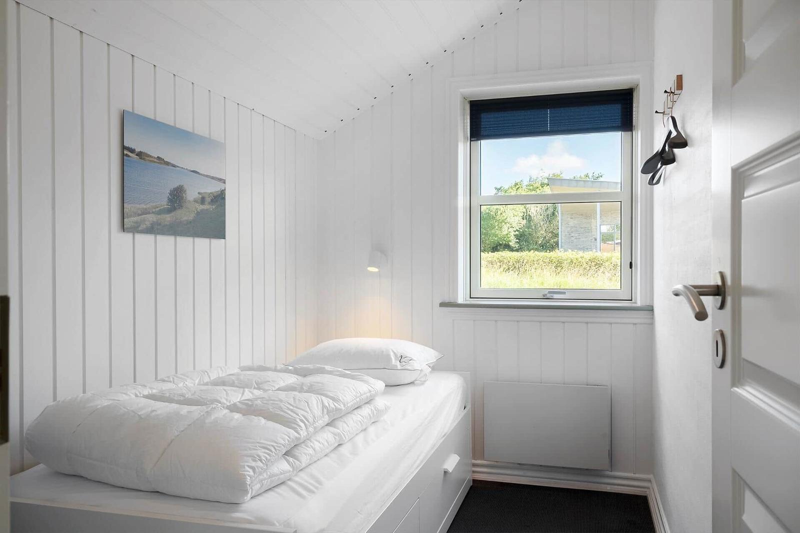 Schlafzimmer mit weißem Bett, Fenster und Wandbild.
