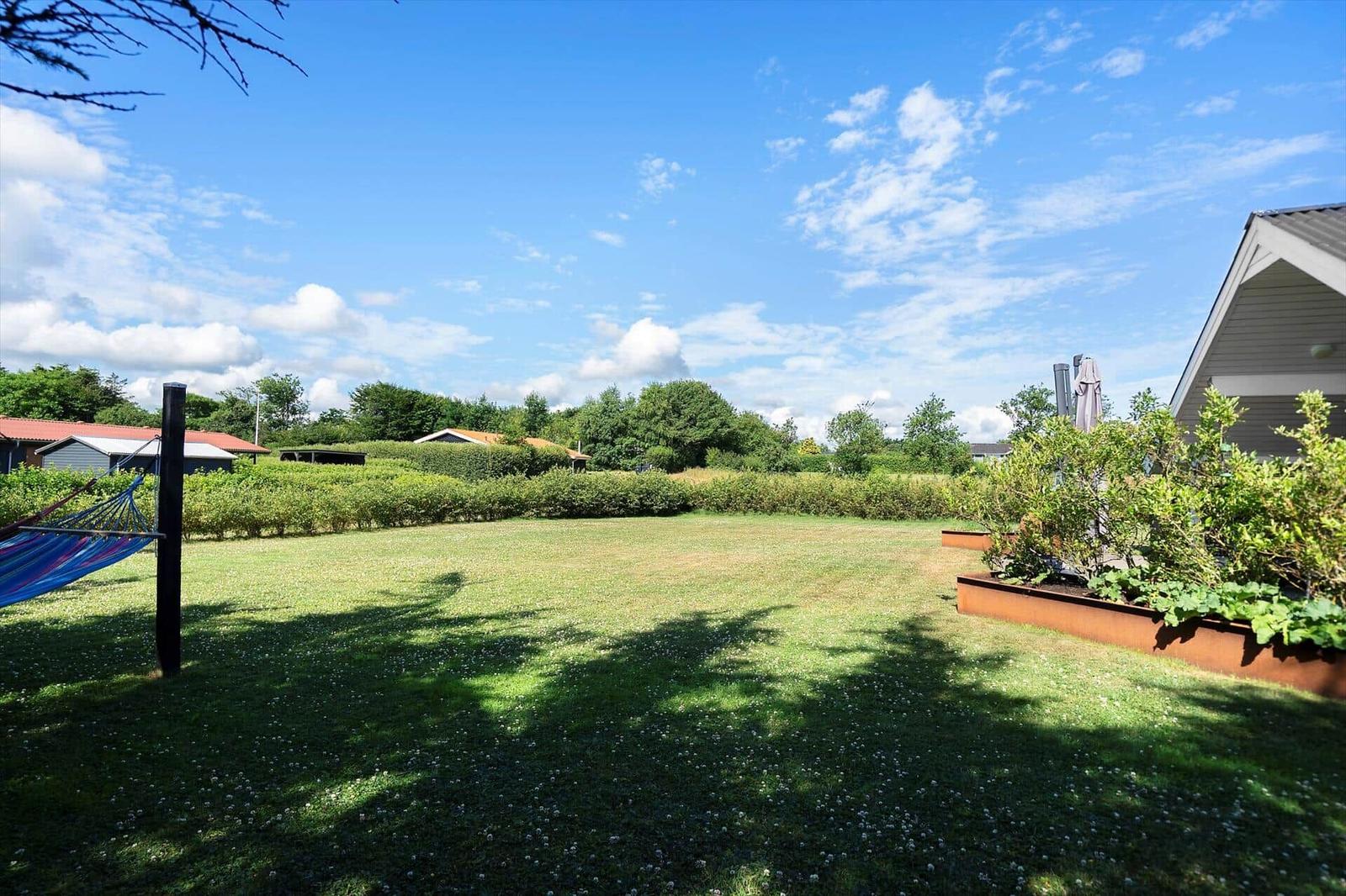 Großer Garten mit Liege, Rasen und Sträuchern unter blauem Himmel.
