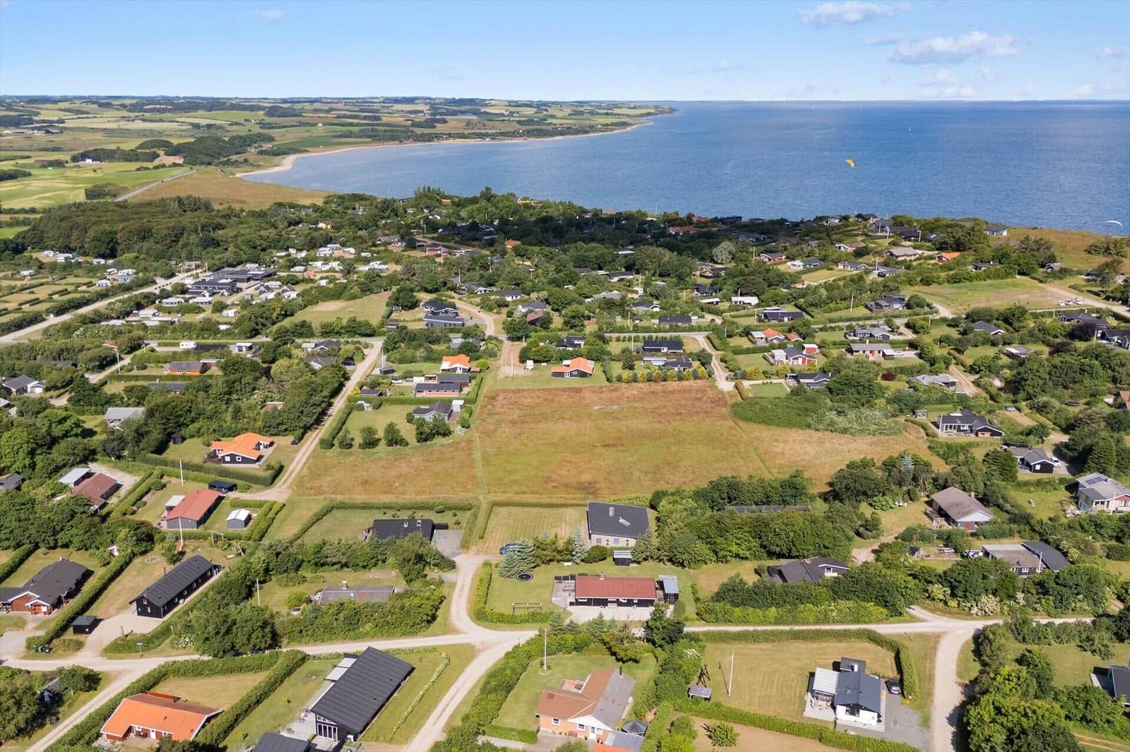 Aerial view of coastal village with houses, greenery, and sea in background.