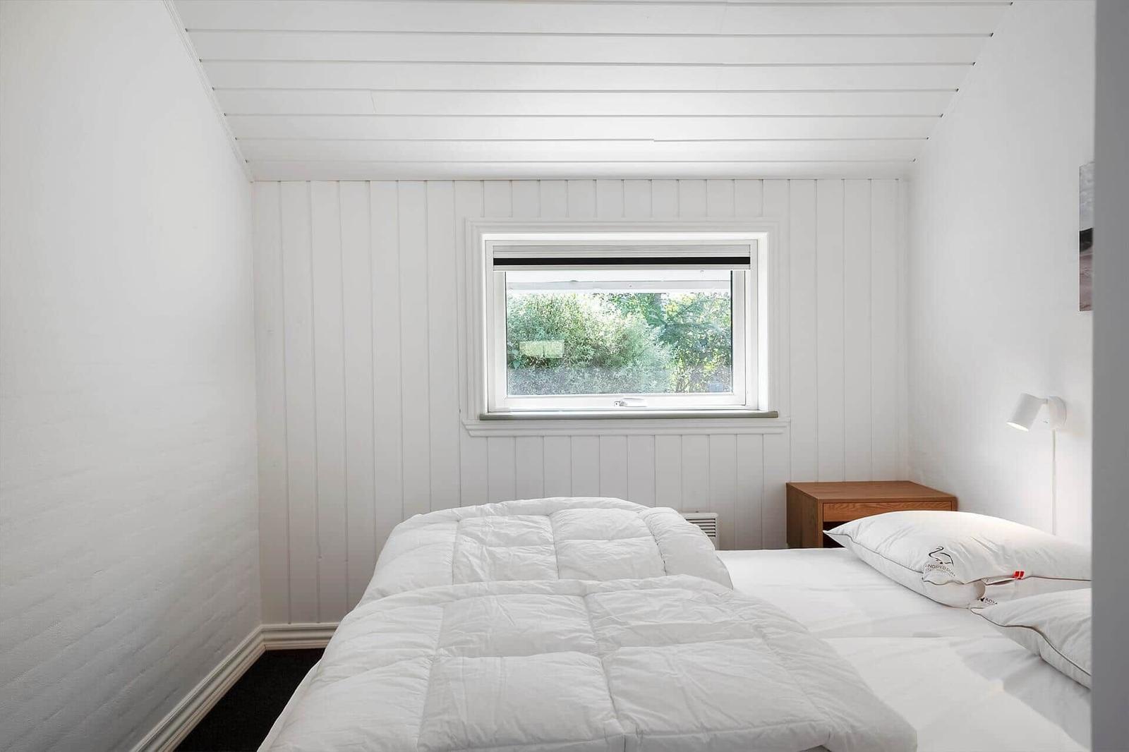 Ein Schlafzimmer mit weißer Wandverkleidung, einem Bett und einem Fenster mit Blick auf Grün.