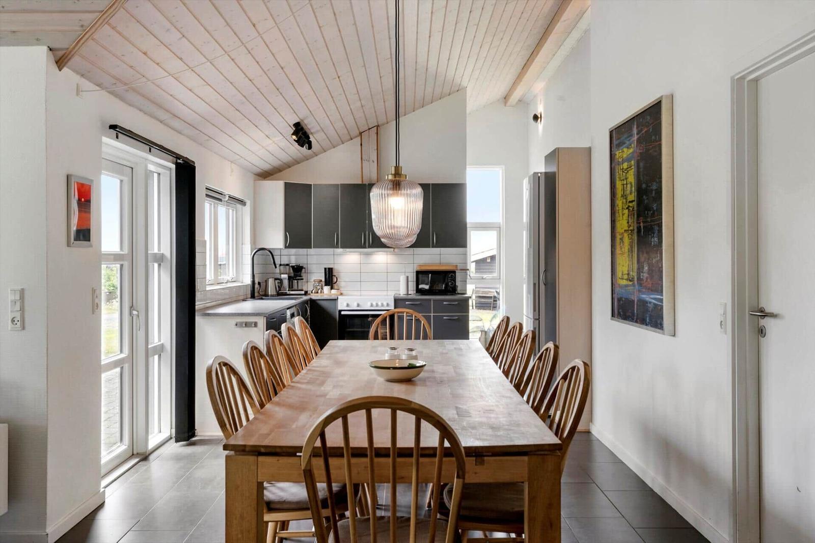 Esszimmer mit Holztisch und Stühlen. Küche mit Schränken und Fenster. Holzdecke und Wandbild.