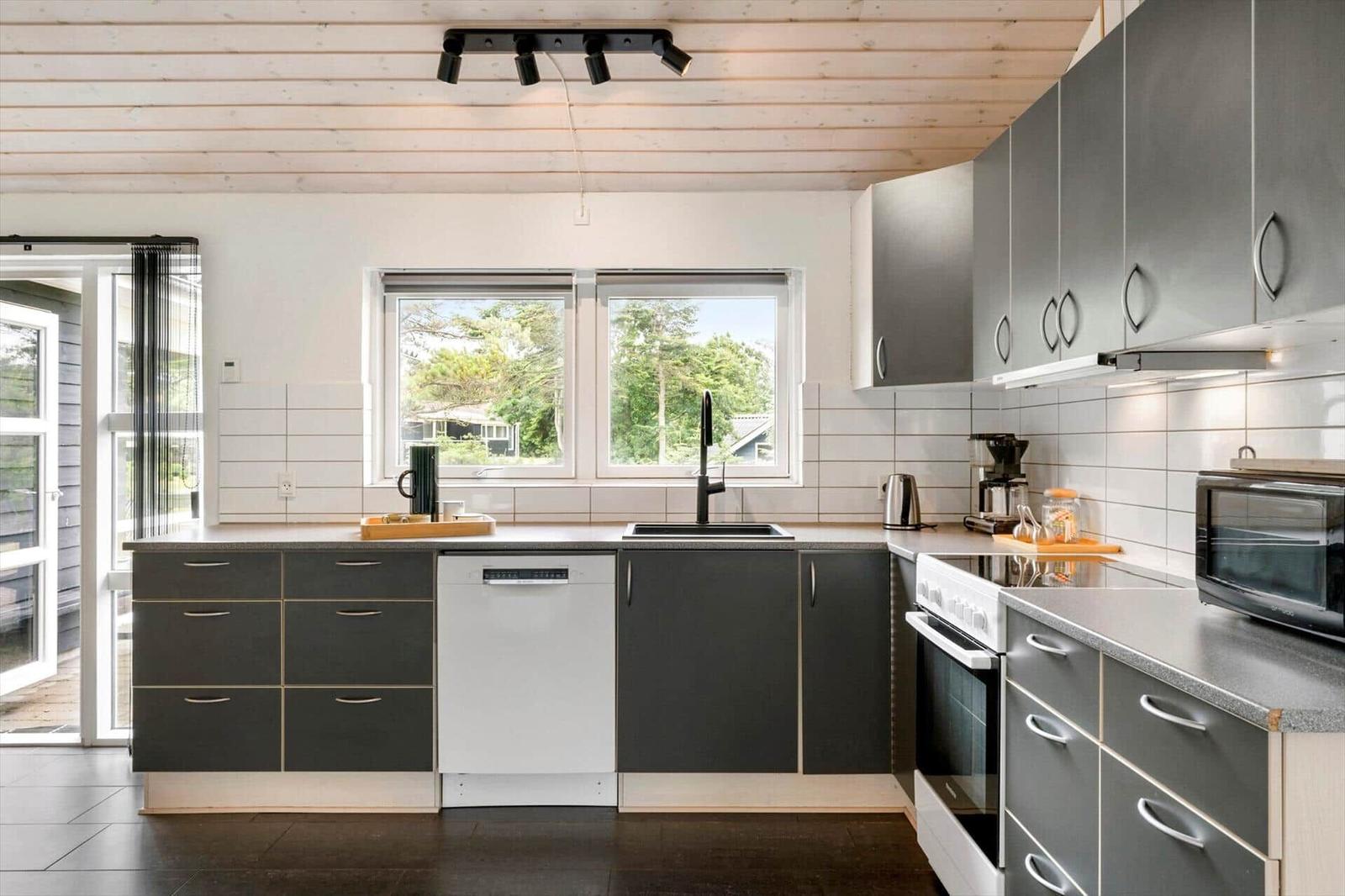 Moderne Küche mit grauen Schränken, Spüle und Fenster zum Garten.