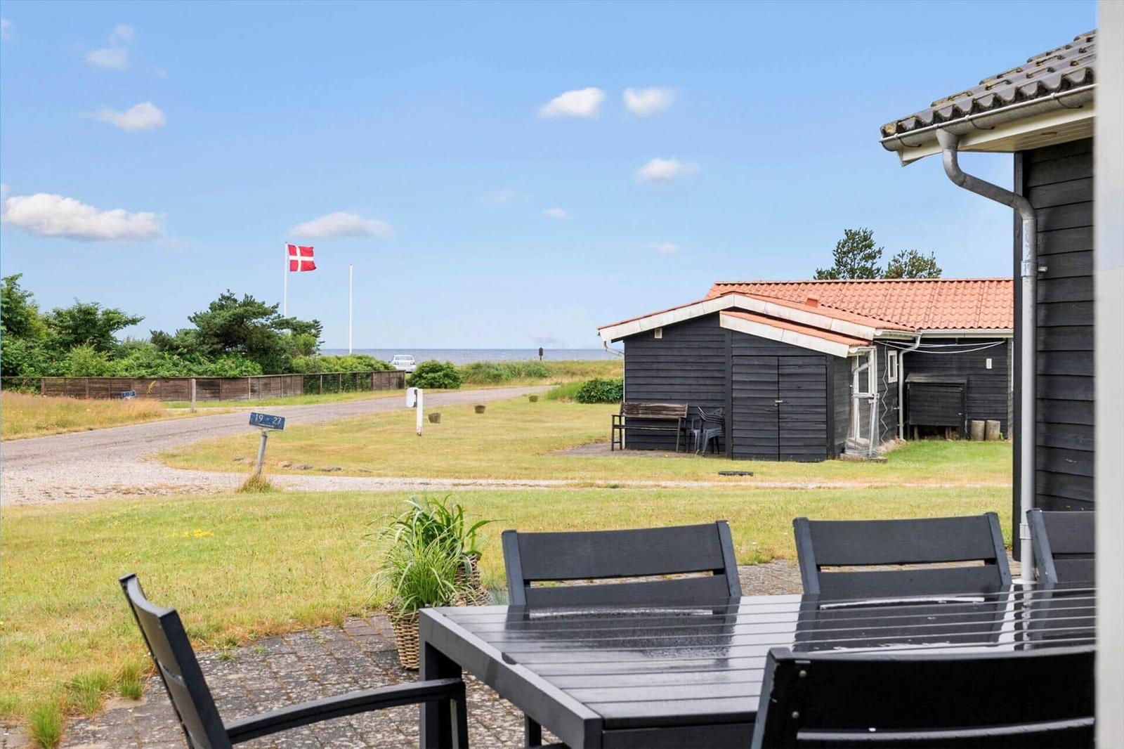 Terrasse mit Tisch und Stühlen, Blick auf Strandhaus und dänische Flagge.