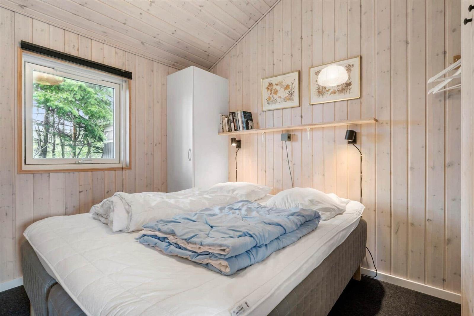 Schlafzimmer mit Bett, Fenster und Holzwandverkleidung.