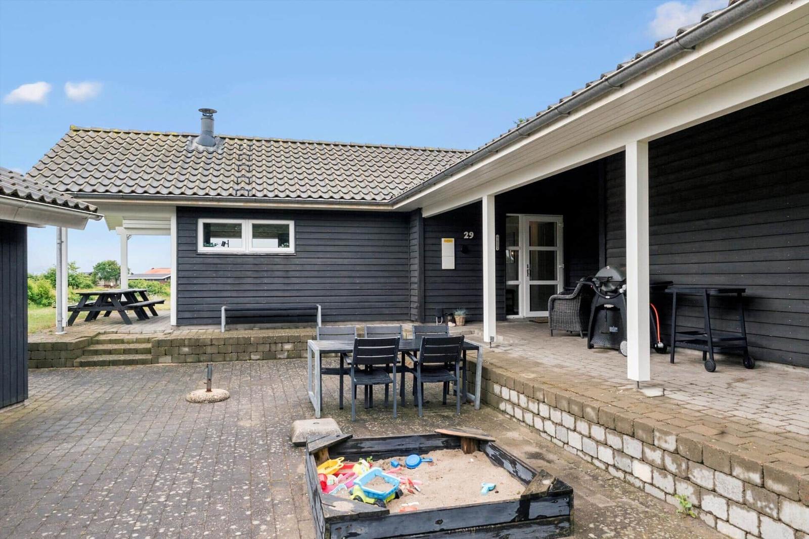 Haus mit Terrasse, Grill, Spielplatz und Tisch mit Stühlen.