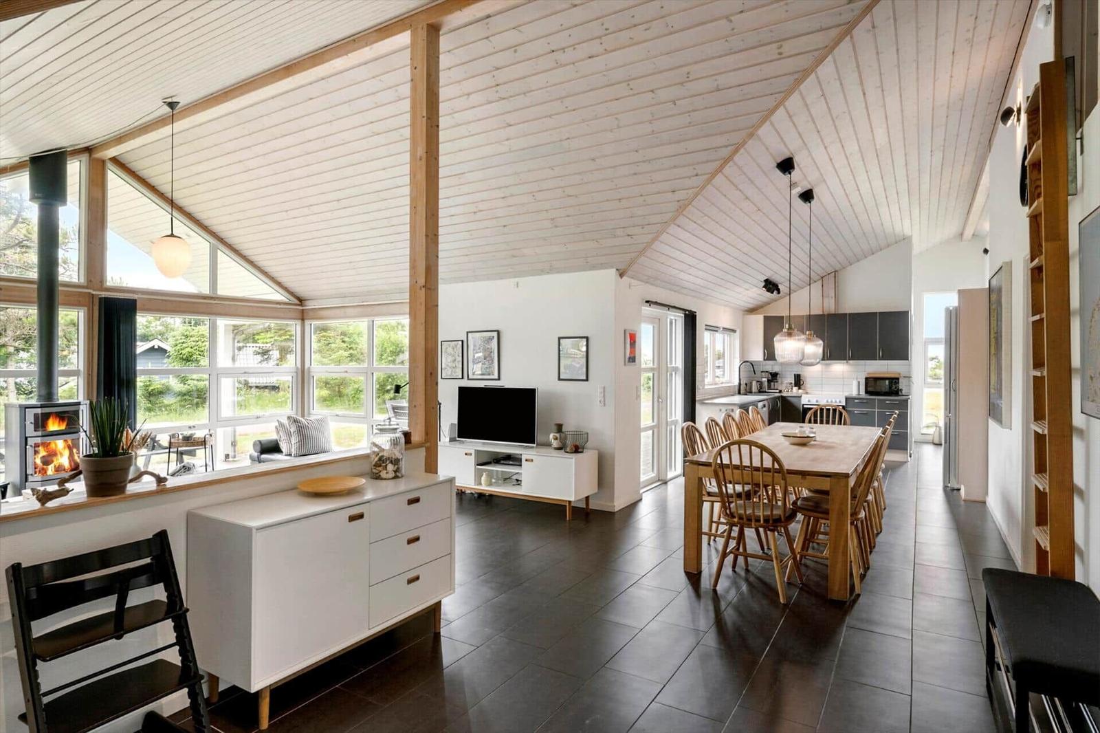 Großes Wohn- und Esszimmer mit Holzdecke, Kamin und moderner Küche.