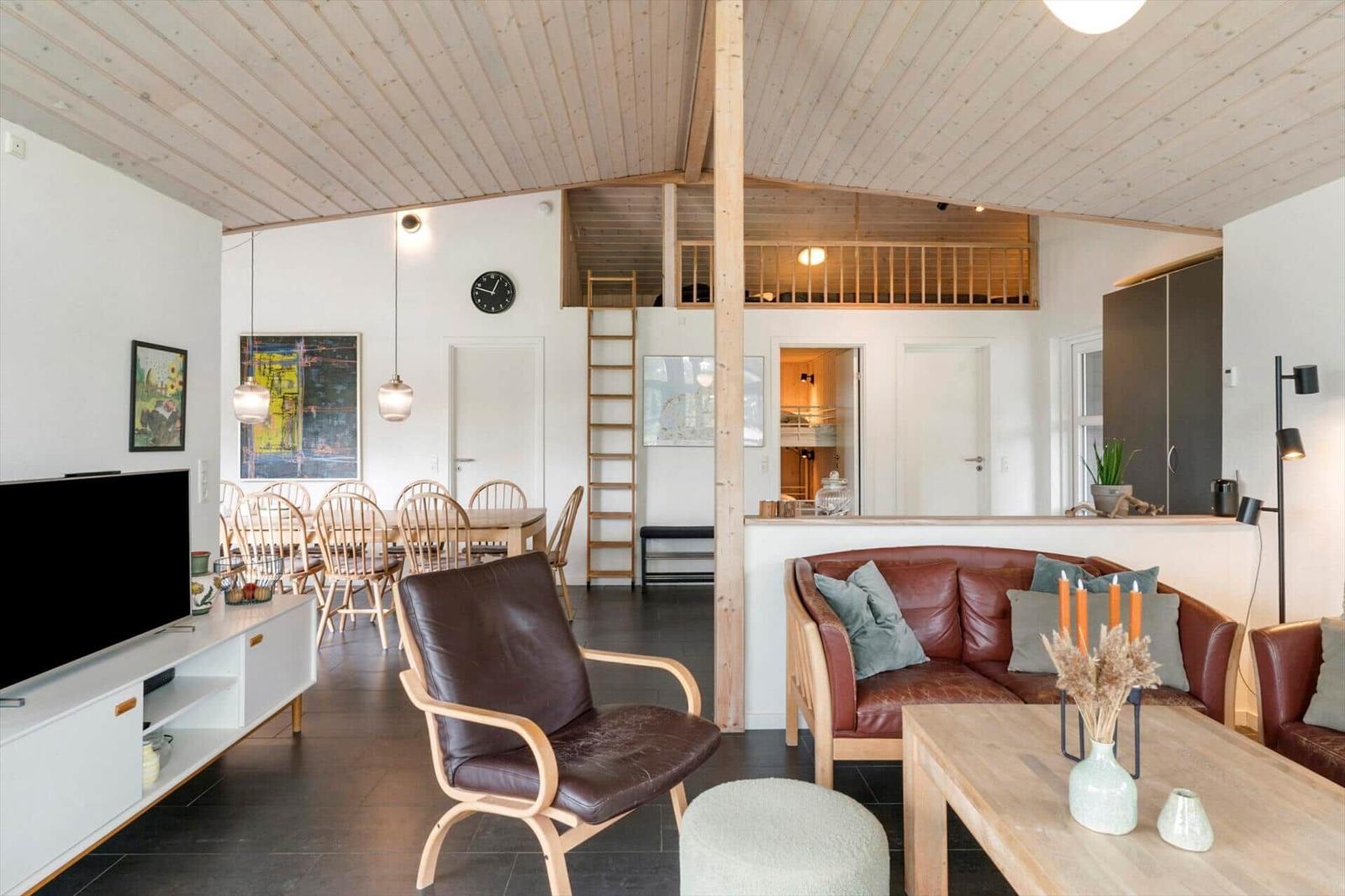 Wohnzimmer mit Essbereich, Sofa, Sessel und Holzdecke. Treppenaufgang zur oberen Etage.