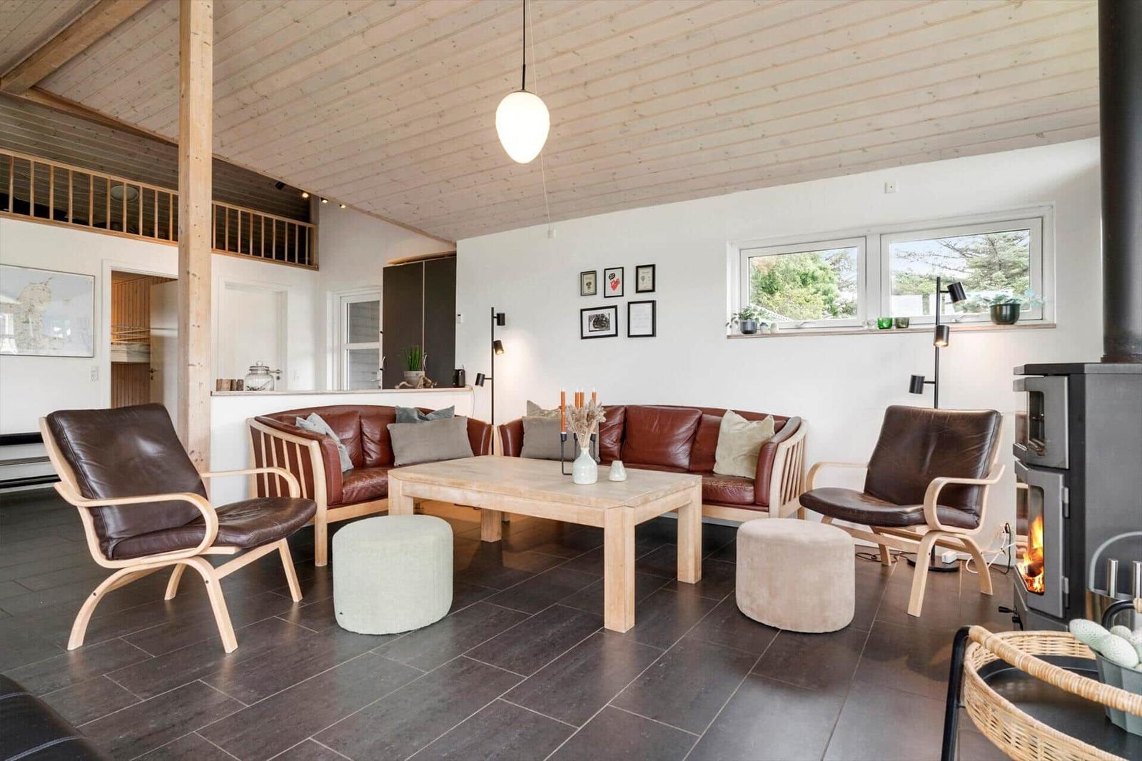 Wohnzimmer mit Holzdecke, Ledersofa, Kamin und Fenstern mit Blick auf Grün.