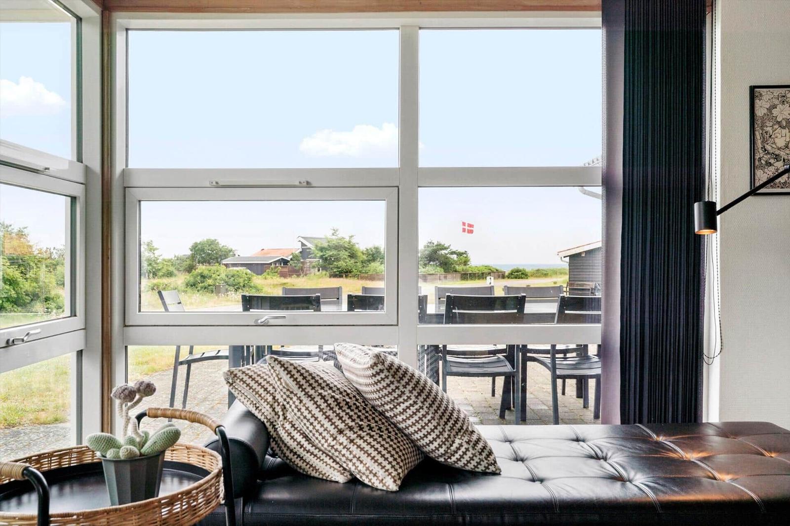Ein schwarzes Sofa mit Kissen vor großen Fenstern mit Blick auf eine Terrasse und Landschaft.