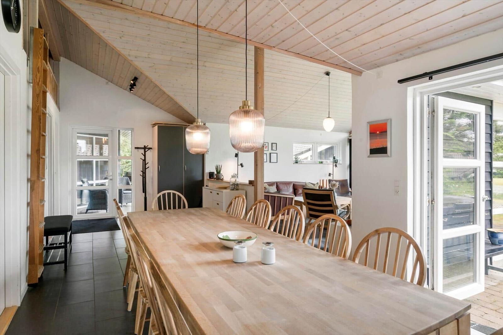 Essbereich mit Holztisch und Stühlen unter Holzdecke. Durchgang zur Wohnküche und Terrasse.