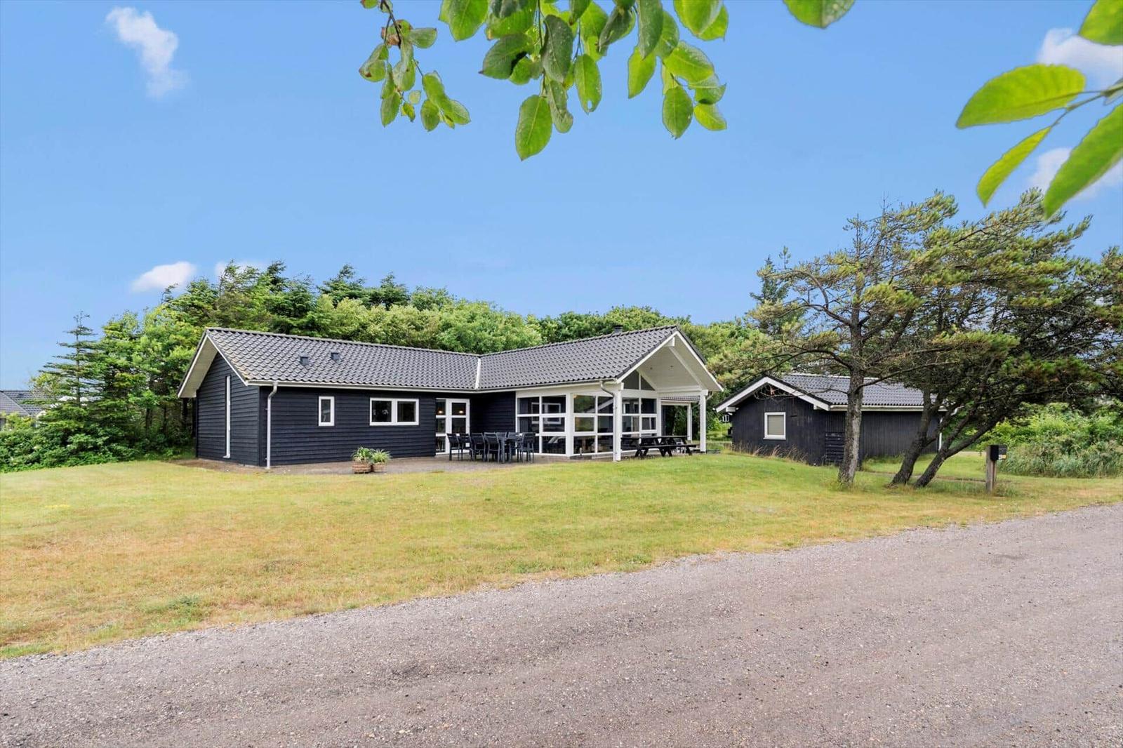 Schwarze Ferienhaus mit Terrasse und Garten. Umgeben von Bäumen und Gras.