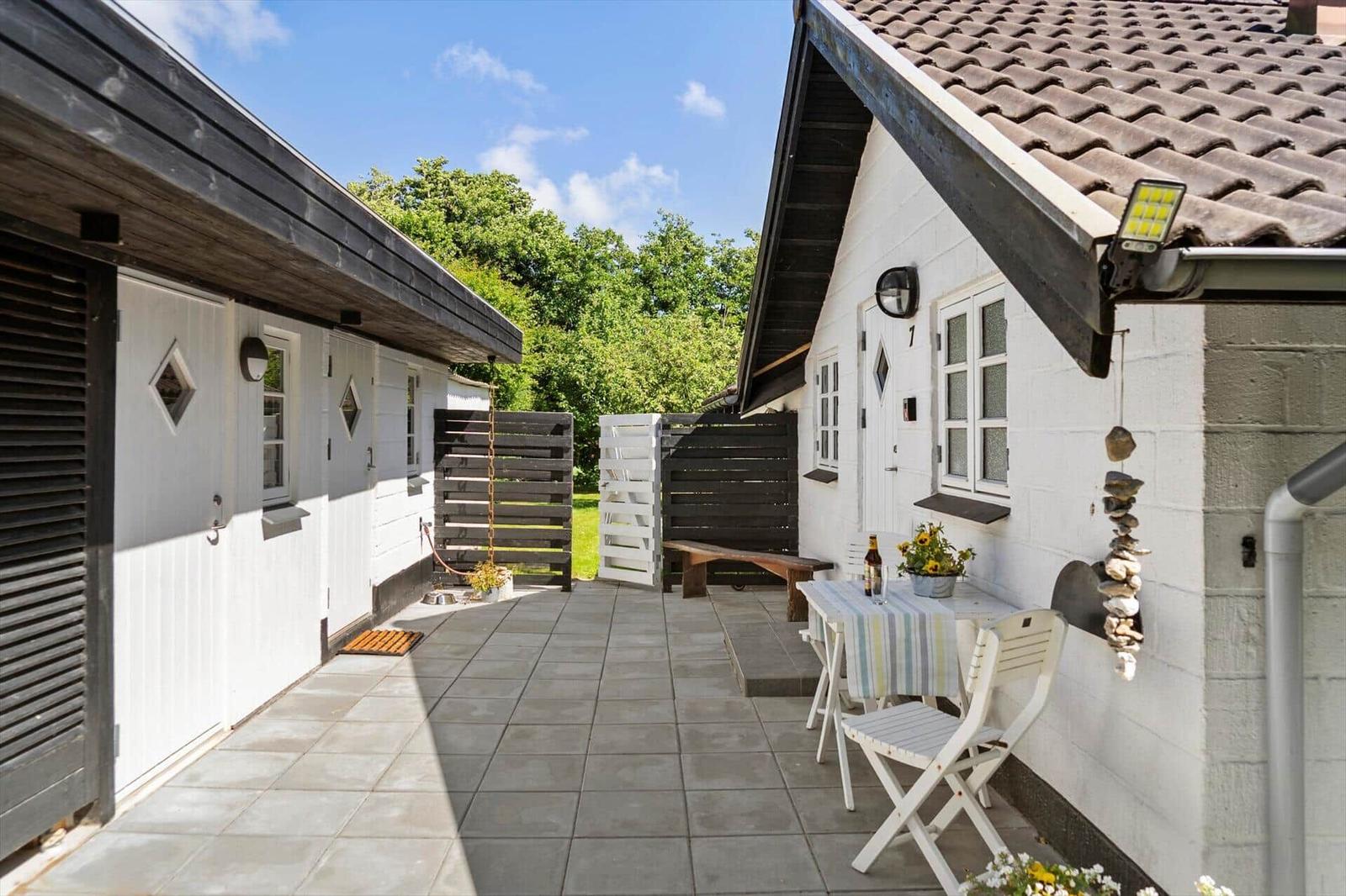 Terrasse mit Tisch, Stühlen und Blumen vor weißem Haus mit Dachgauben.