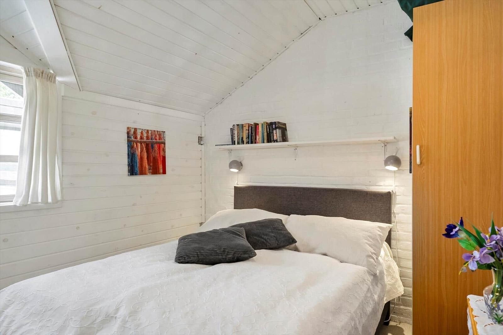 Schlafzimmer mit Bett, Bücherregal und Fenster.