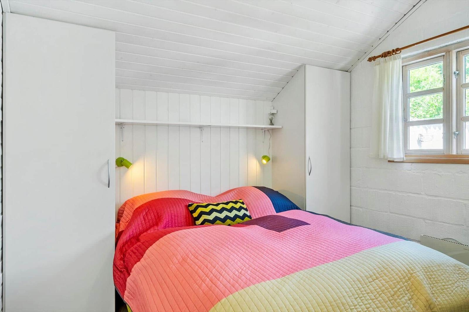 Schlafzimmer mit Bett, weißen Schränken und Fenster. Decke und Wände weiß. Decke mit Holzverkleidung.