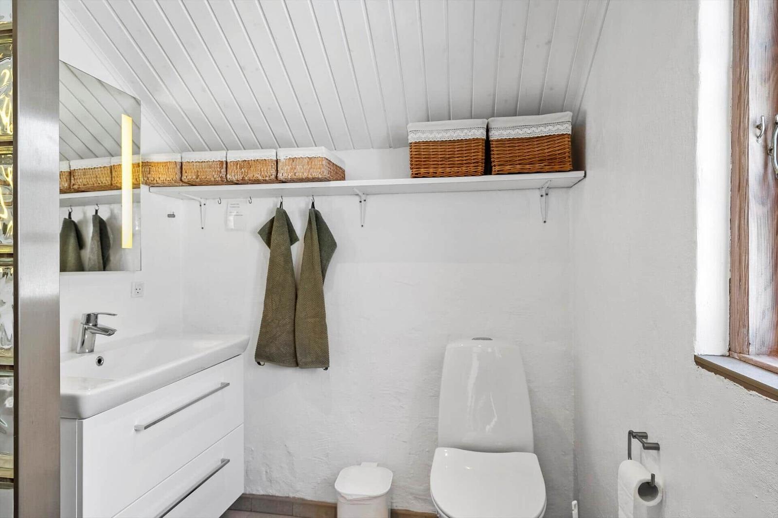 Badezimmer mit Toilette, Waschbecken und Regal mit Körben.