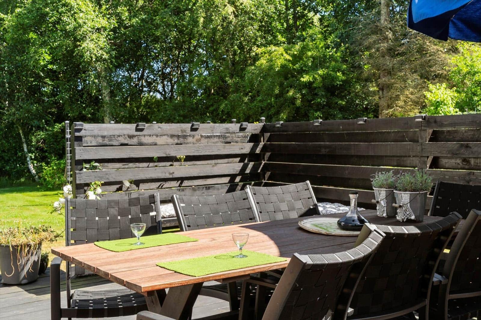 Holztisch mit Stühlen und Pflanzen auf einer Terrasse mit Holzgeländer.