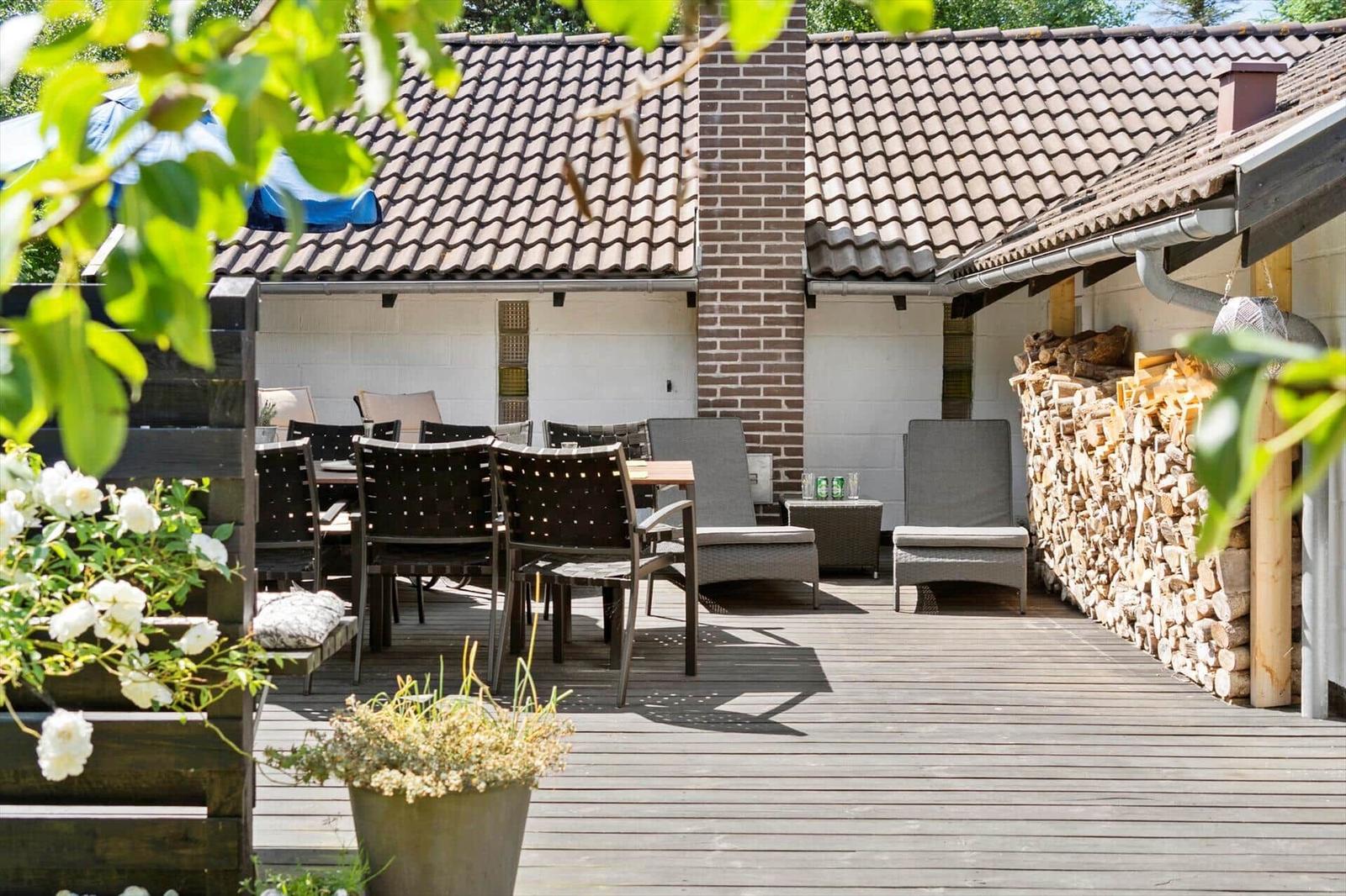Terrasse mit Holzdielen, Gartenmöbeln und Holzstapel an der Wand.