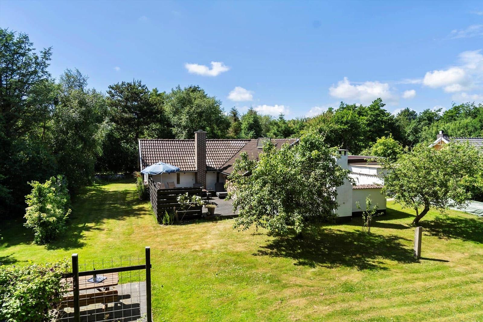 Haus mit Garten, Terrasse und Grillplatz unter blauem Himmel.