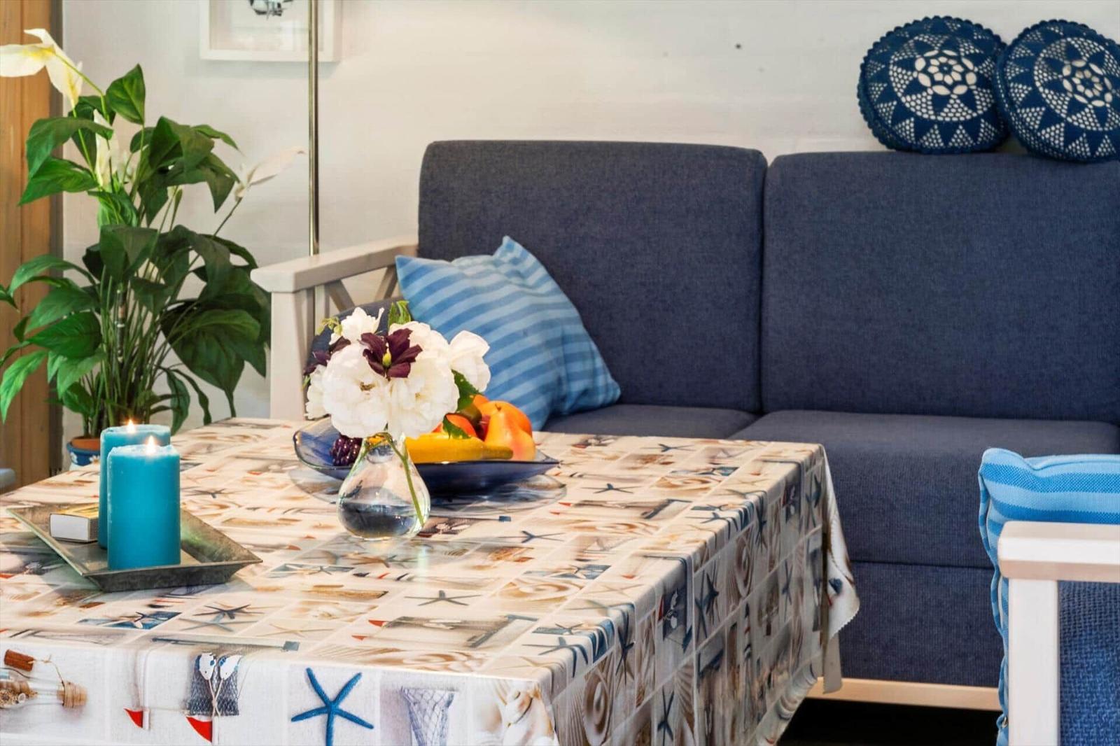 Ein Tisch mit Tischdecke, Blumen und Obst vor einem Sofa mit Kissen.