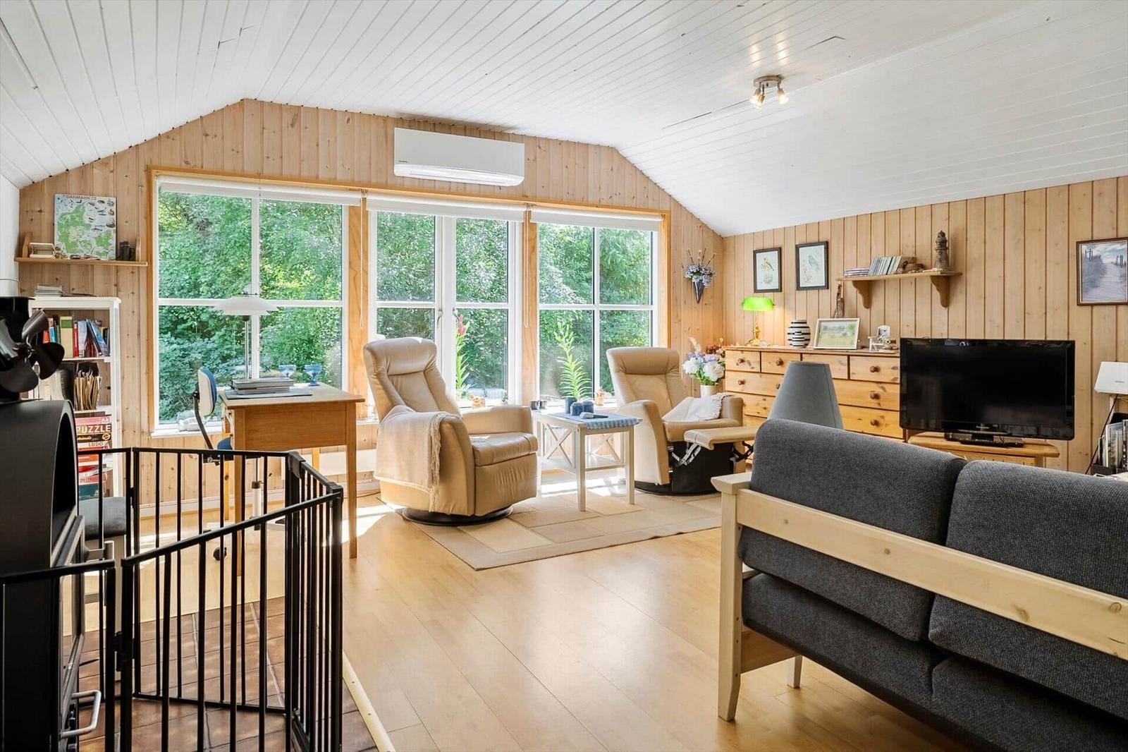 Wohnzimmer mit Holzwand, Fenster, Sofa, Sessel und Fernseher.