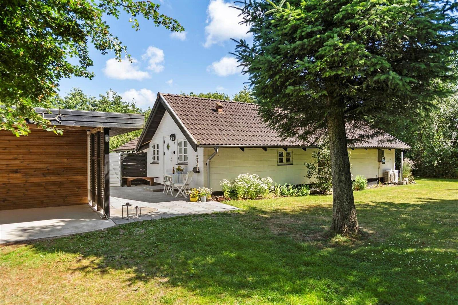 Wohnhaus mit Garten, Terrasse und Holzgarage unter Bäumen.