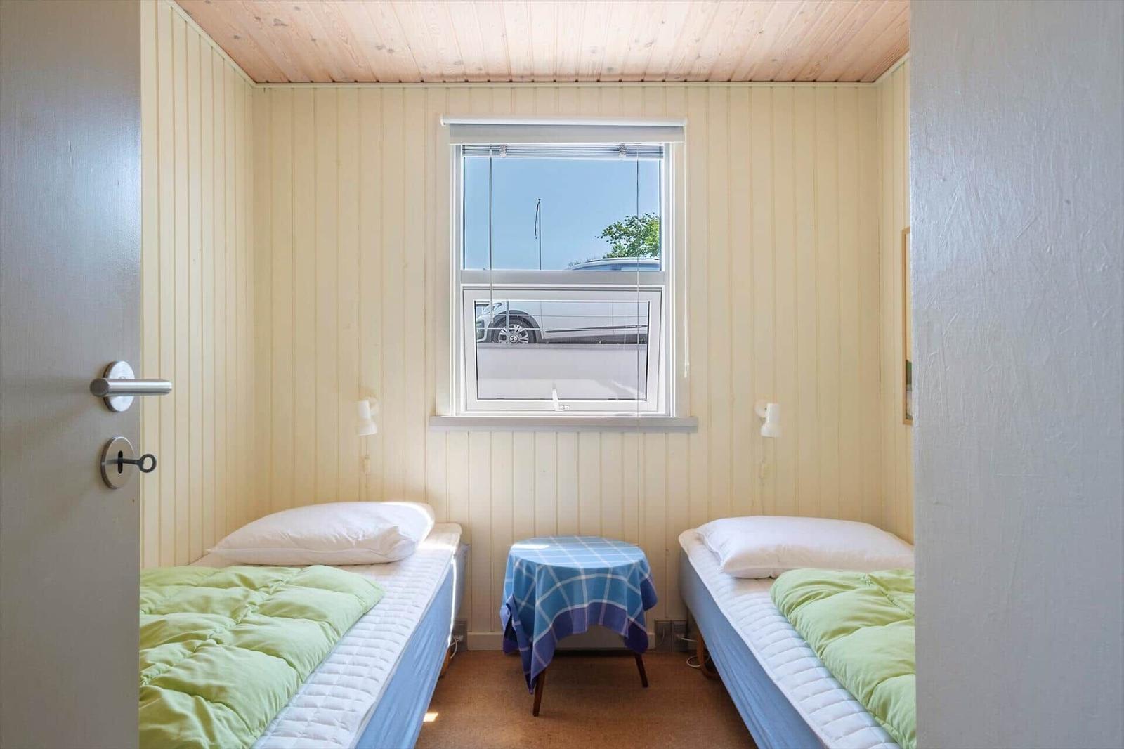 Zwei Einzelbetten mit grünen Decken, ein Tisch mit Tischdecke und ein Fenster.