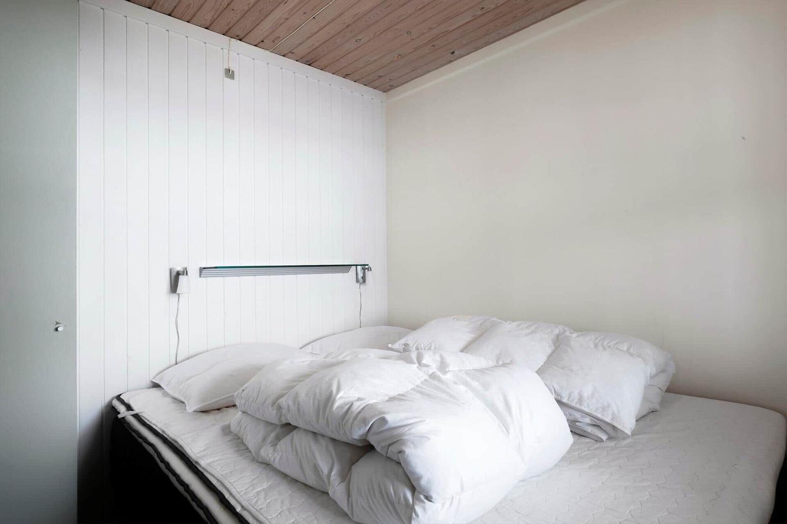 Ein Bett mit weißen Kissen und Decke, Wand mit vertikalen weißen Paneelen und Holzdecke.