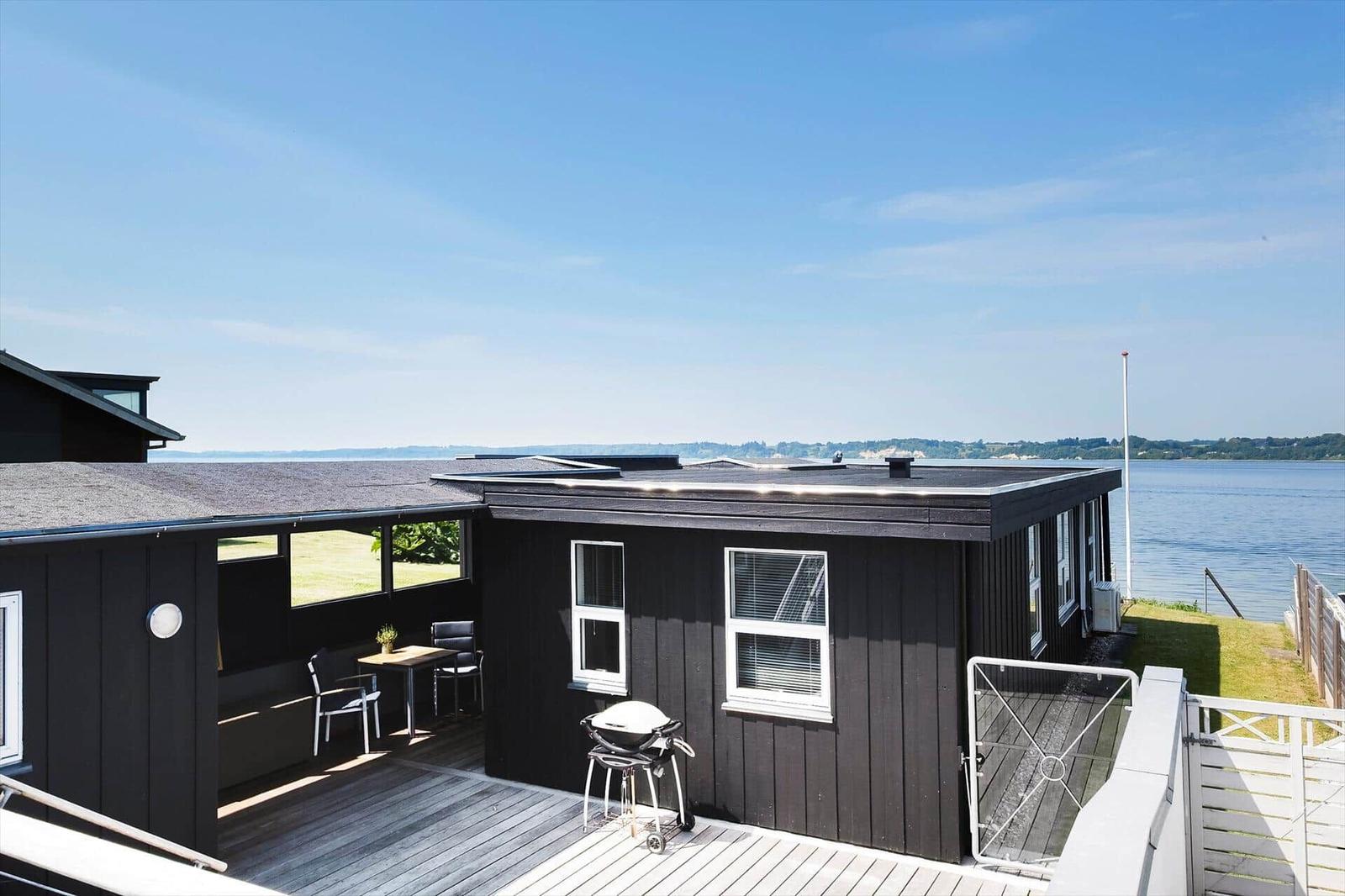 Schwarzes Haus mit Terrasse, Grill und Blick auf Wasser.