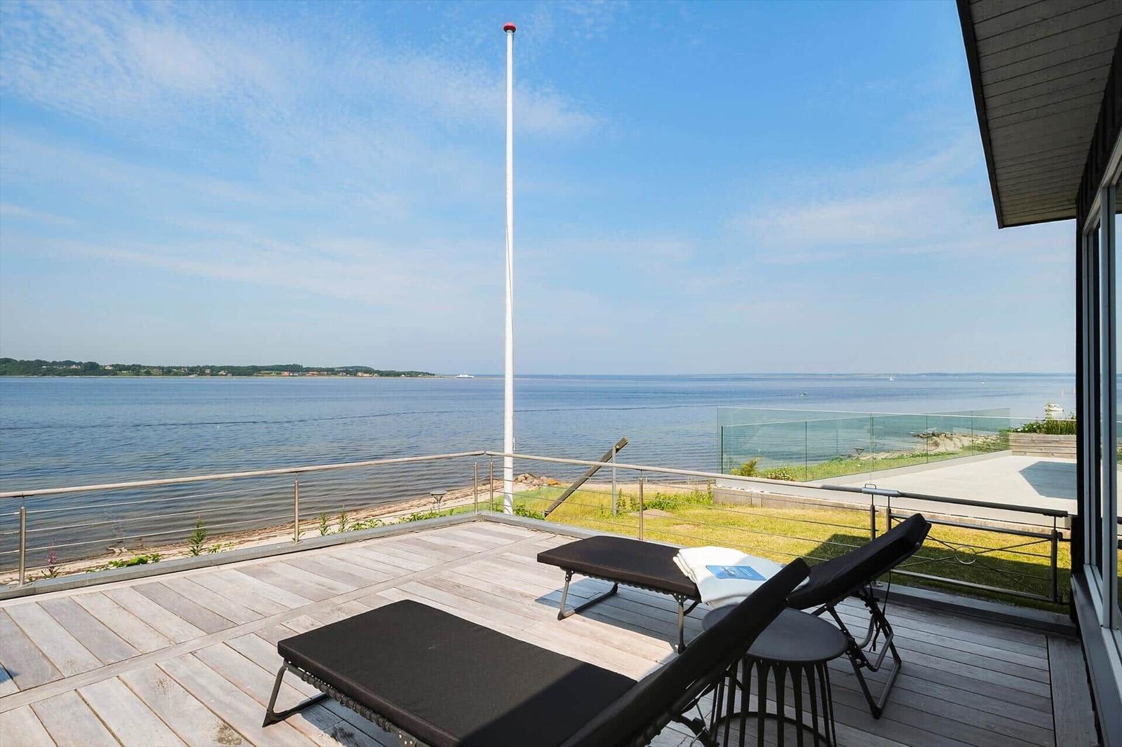 Terrasse mit Liegen und Blick aufs Wasser. Hoher Mast und Glasgeländer.