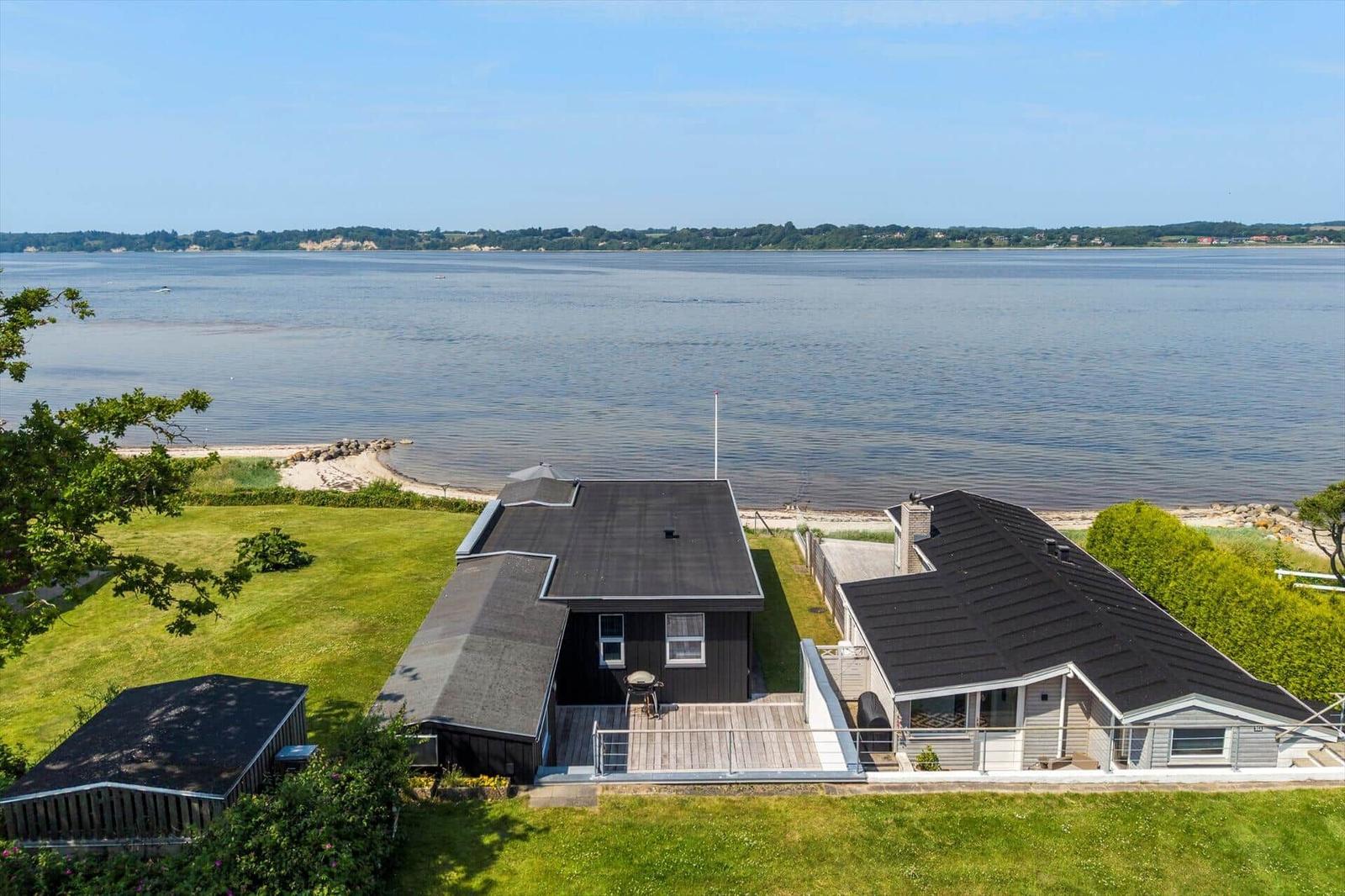 Haus mit Terrasse am Wasser, umgeben von Grünfläche und Blick auf die Bucht.