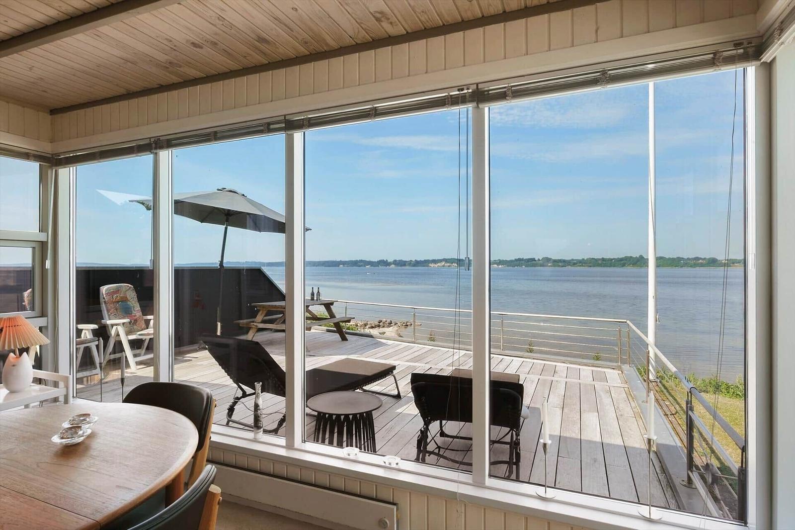 Große Glasfront mit Blick auf den See und Terrasse mit Liegestühlen und Sonnenschirm.