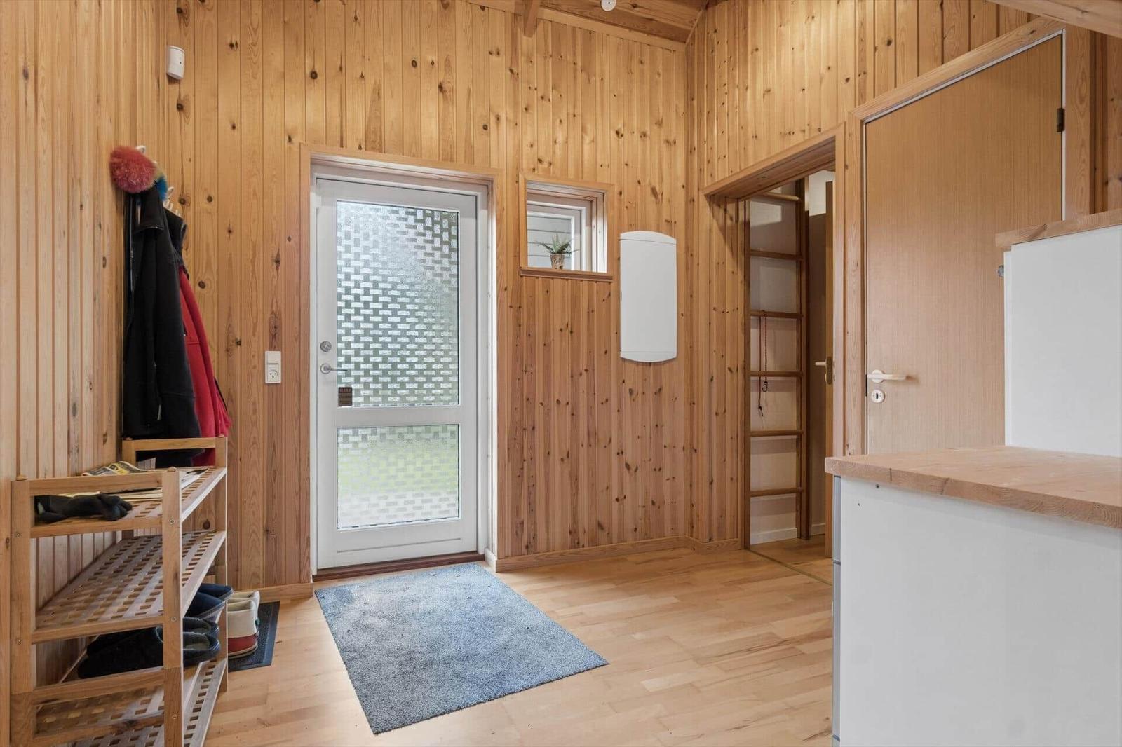 Eingangsbereich mit Holzwand, Tür, Schuhregal und Küchenzeile.