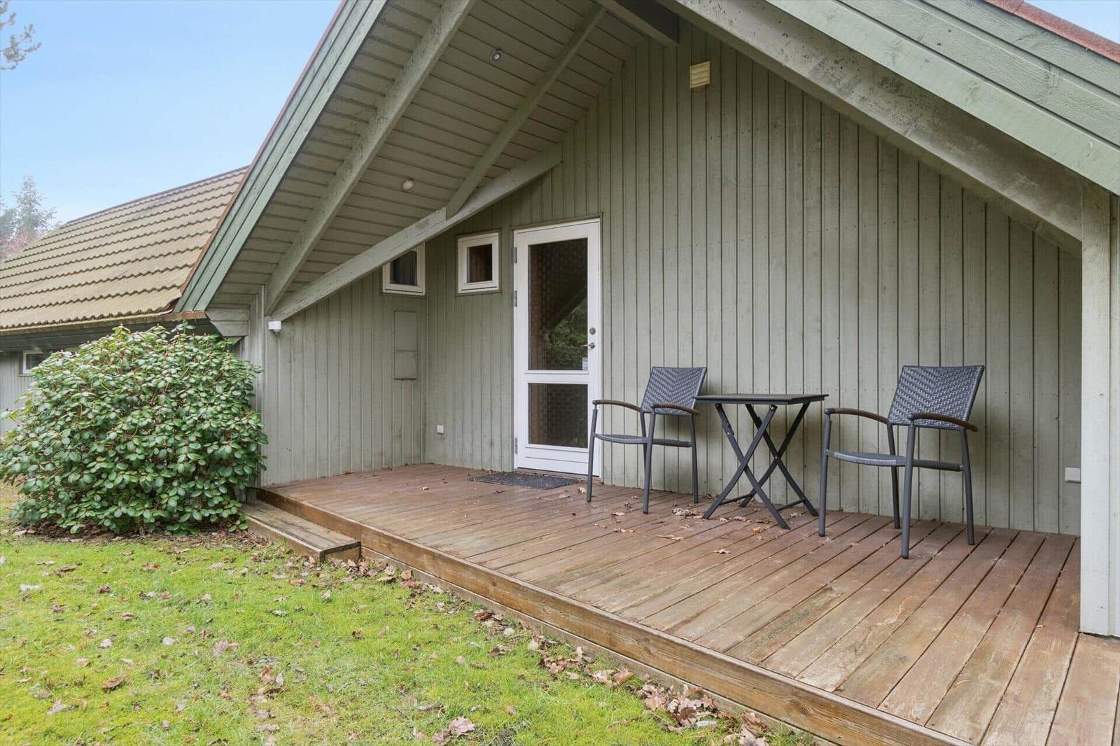 Terrasse mit Tisch und zwei Stühlen vor einem Holzhaus mit Eingangstür.