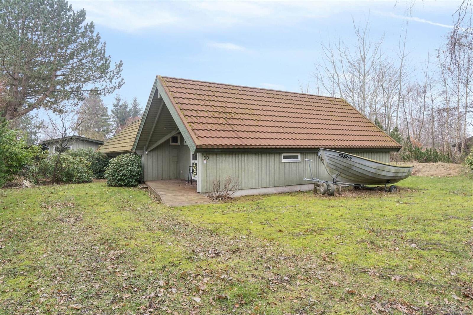Ein kleines Haus mit braunem Dach und Holzveranda. Ein Boot steht auf einem Anhänger im Gras.