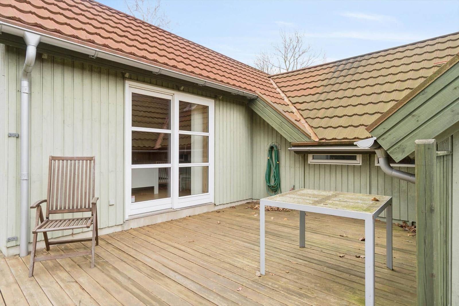 Terrasse mit Holzdecke, Stuhl und Tisch vor einem Haus mit weißen Fenstern und rotem Dach.