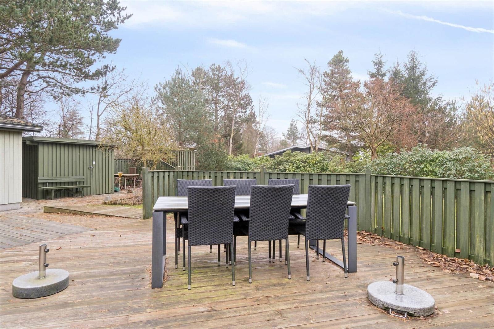 Terrasse mit Esstisch und Stühlen, umgeben von Grünfläche und Zaun.
