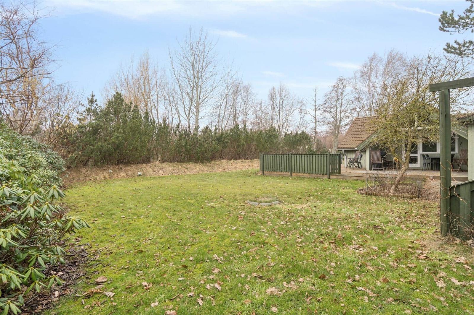Grüner Garten mit Holzgeländer und Terrasse. Im Hintergrund Bäume und ein Haus.