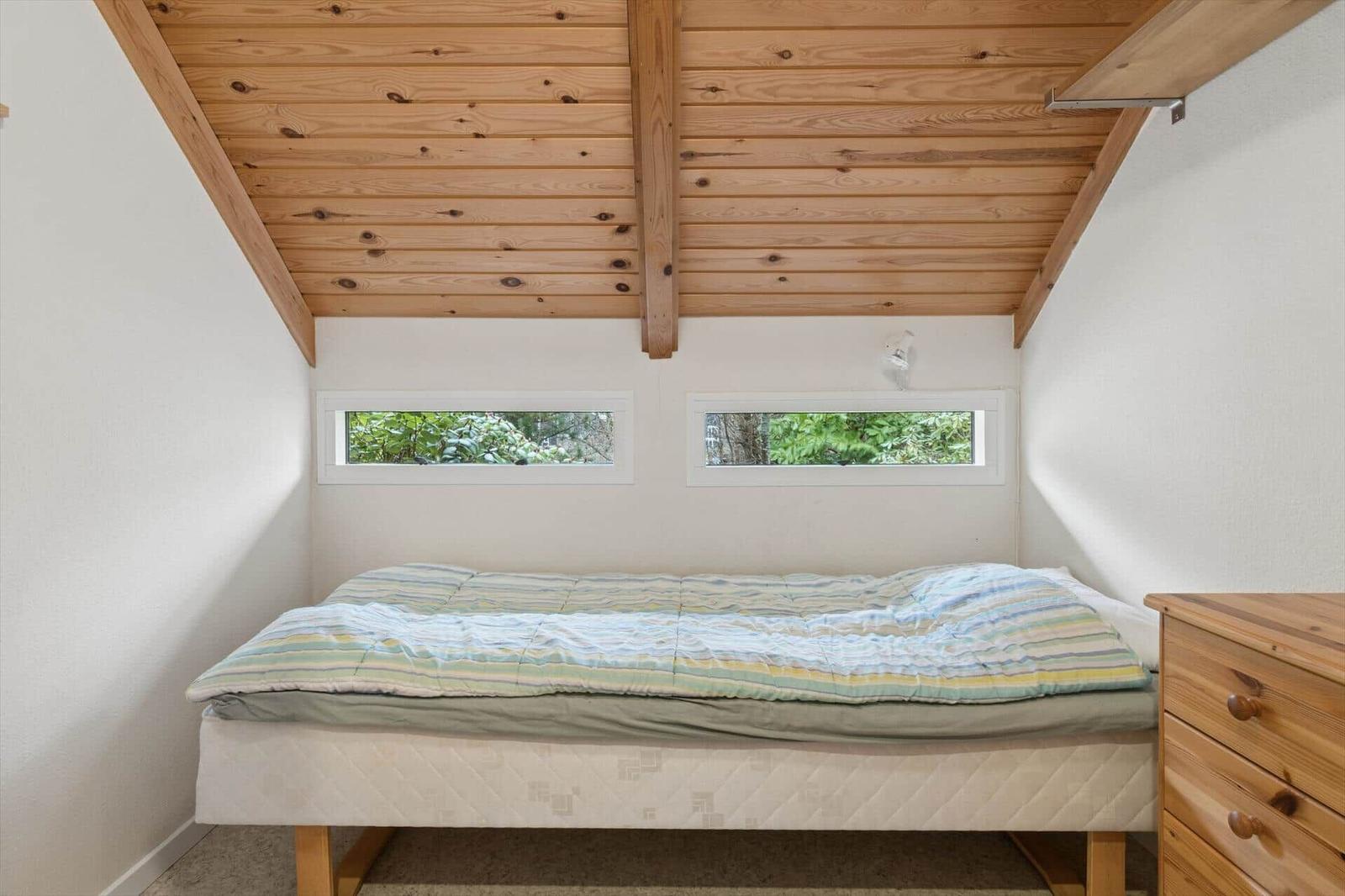Schlafzimmer mit Holzdecke, zwei Fenstern und einem Bett mit Matratze.