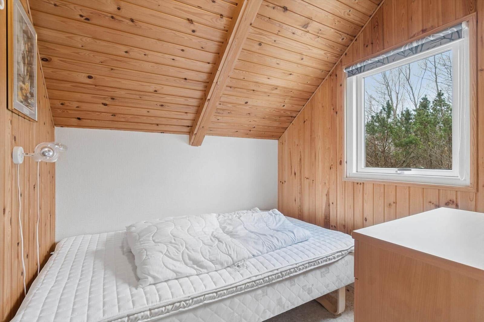 Schlafzimmer mit Holzwänden, Bett und Fenster zur Aussicht.